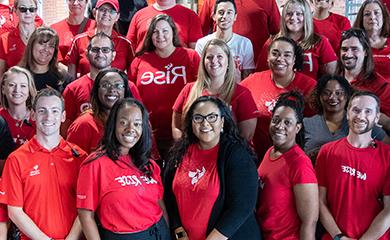 A group photo of alumni in University of Phoenix shirts smiling at camera